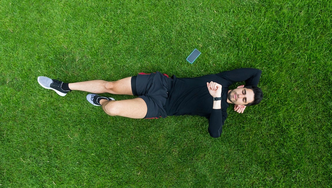 Jogger lying in grass looking on watch.