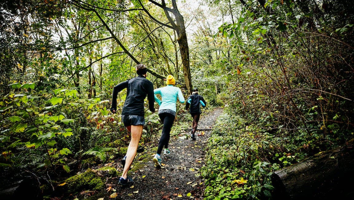 Group of female friends running up forest trail on rainy afternoon.