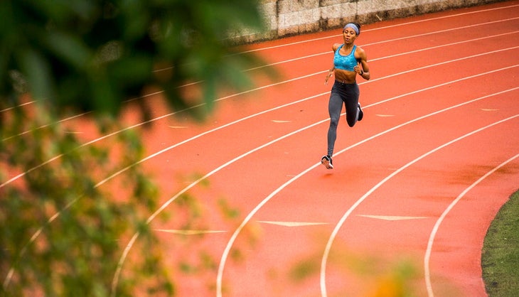 Woman running on track in blue sports bra and black tights with blue headband.