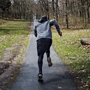 Full length rear view of determined male athlete jogging on narrow street in forest.