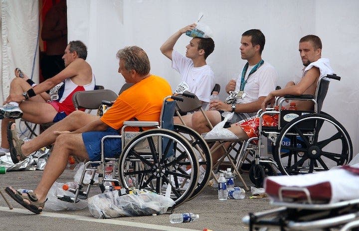 Runners sit in wheelchairs in medical tent, looking overheated and holding icepacks