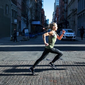 Side view of female athlete running on city street during sunny day in NYC.