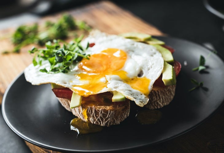 Breakfast toast with avocado, egg and sprouts on a black plate, selective focus.