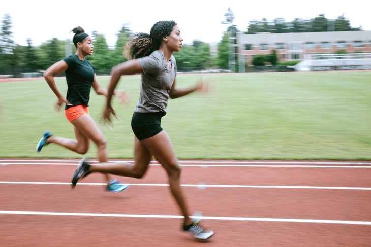 Young adult women sprint down the track, their motion intentionally blurred to show their speed. Training for track and field competition.