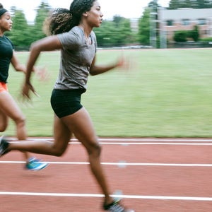 Young adult women sprint down the track, their motion intentionally blurred to show their speed. Training for track and field competition.