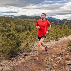 Man in bright red shirt running in the mountains.