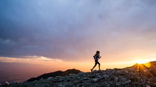A woman trail running at as sunset along a mountain pass.