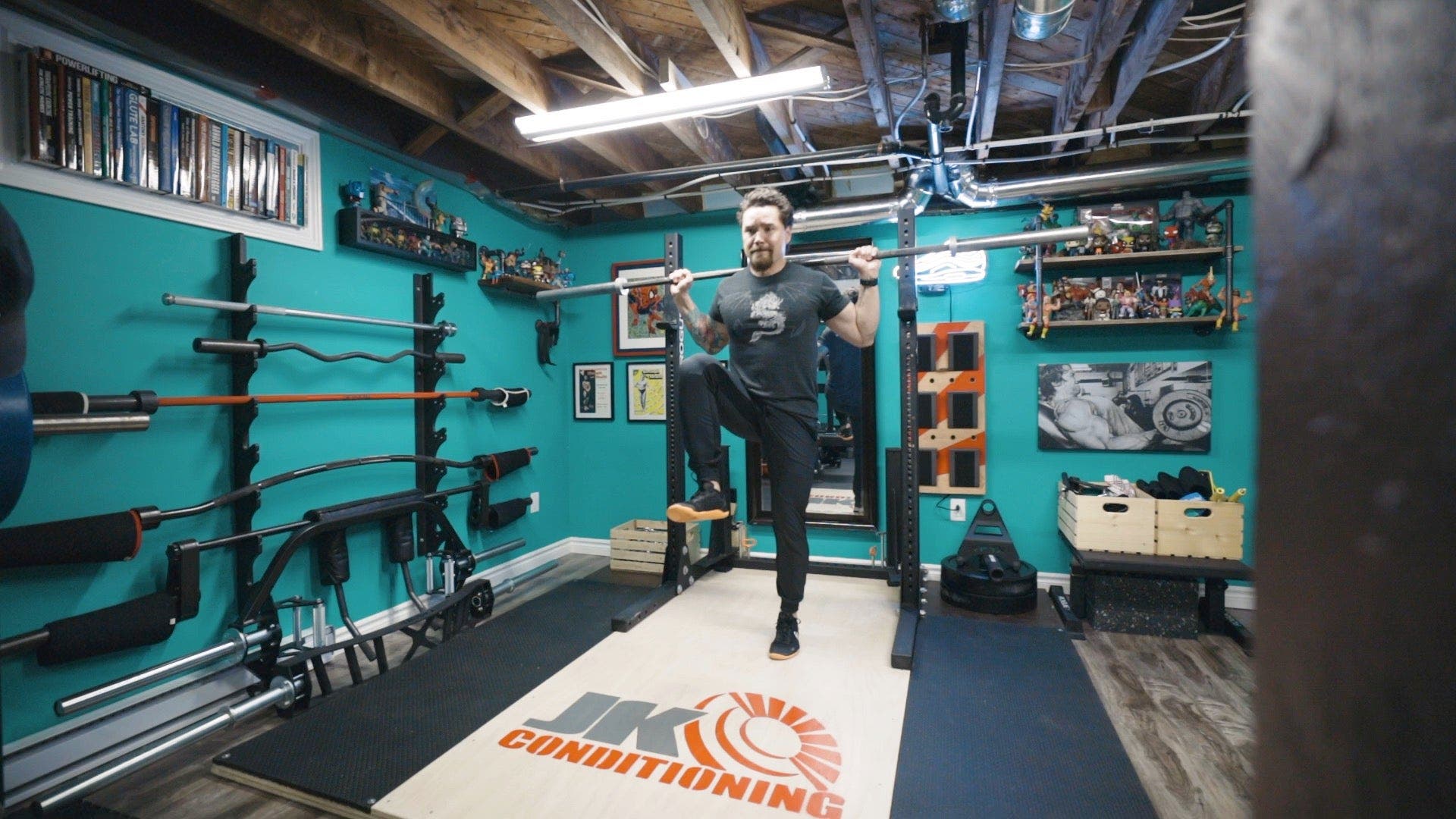 Man in weight room lifting his leg up with knee high quick with barbell on shoulders.