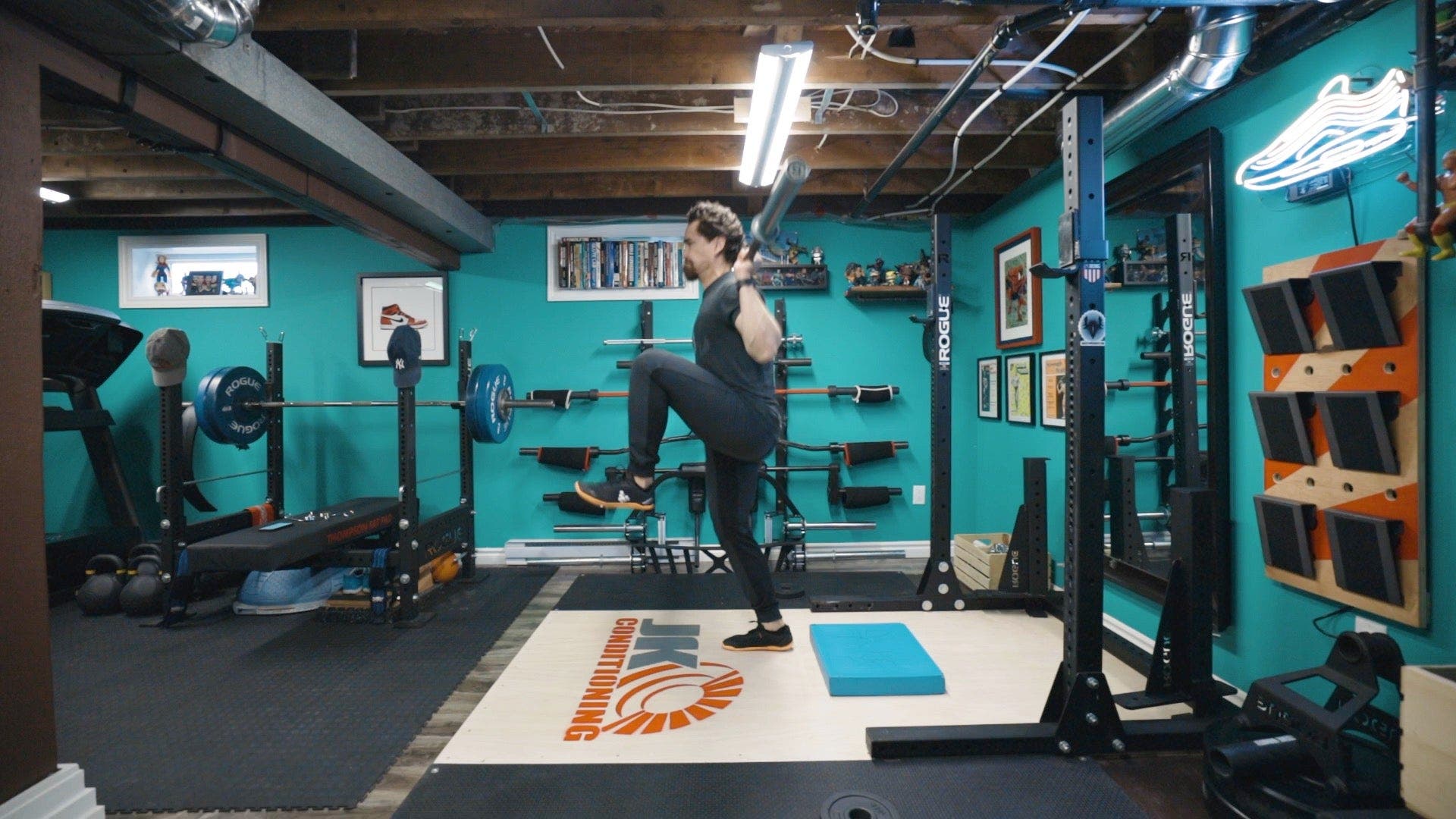 Man with barbell across upper back lifting one knee high.
