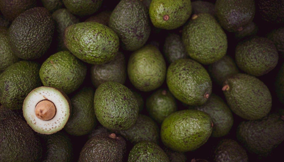 Pile of whole avocados with one sliced in half.
