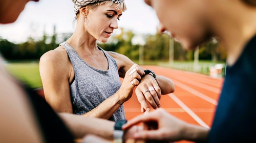Runners checking their times after a speed workout on an outdoor track.