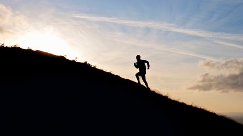 lone runner in silhouette going uphill