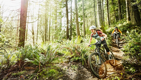 friends riding mountain bikes down trail