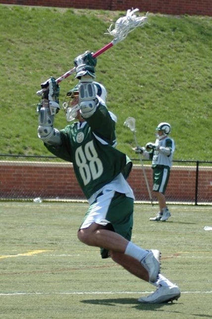 Boy in green lacrosse uniform and helmet playing lacrosse. 
