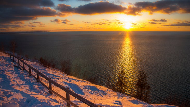 The sun sets over the water and a winter landscape.