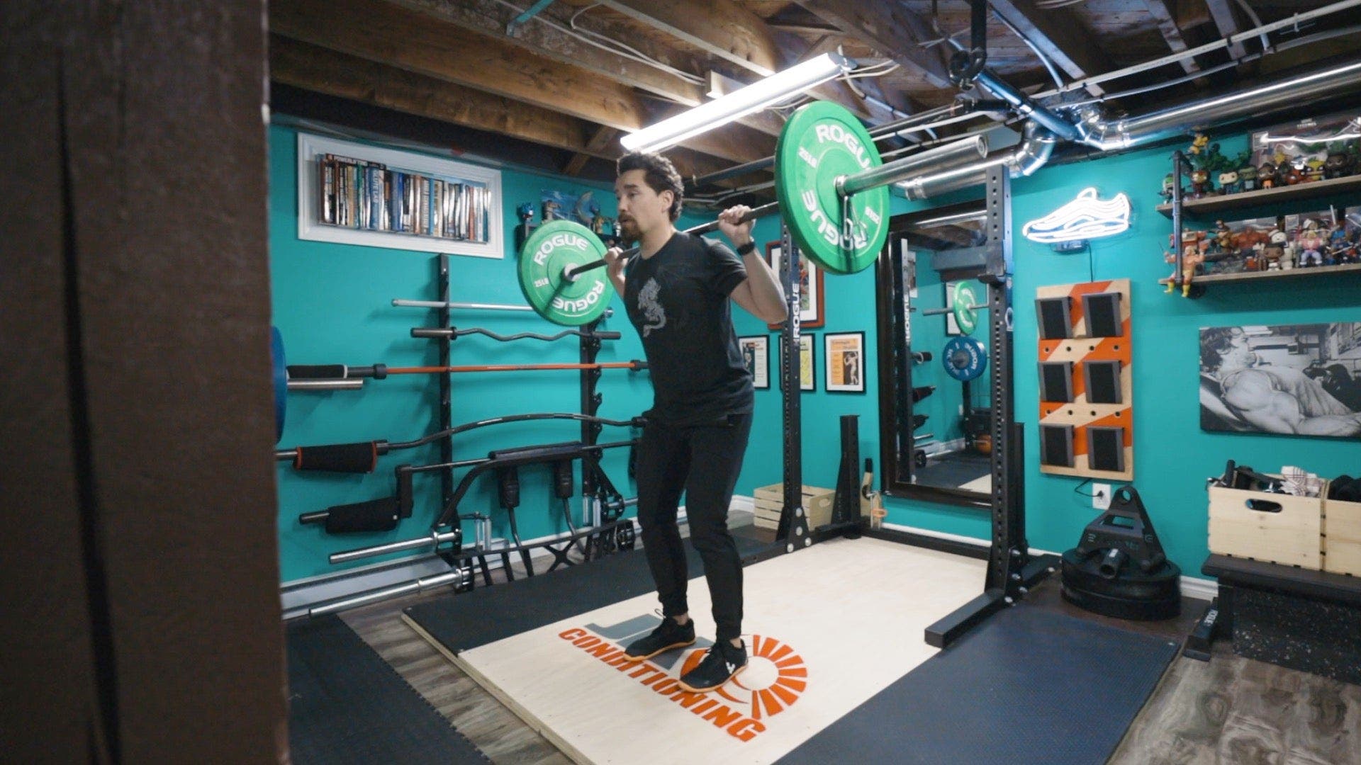Man in weight room lifting barbell behind neck while standing slightly leaned over, both feed on ground.