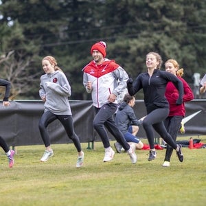 Girls running together with male coach doing strides.