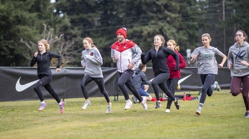 Girls running together with male coach doing strides.