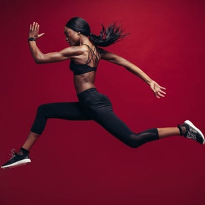 Female athlete running and jumping against red background.