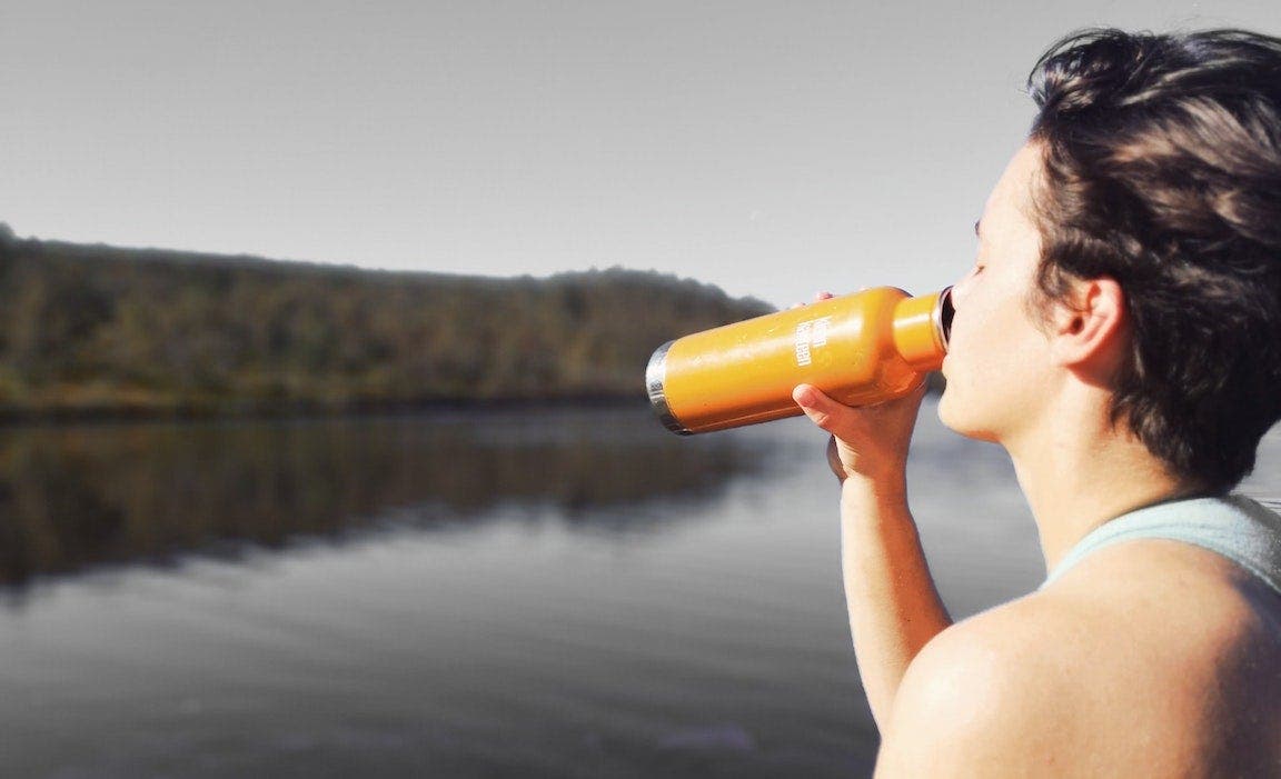Person drinking water overlooking a lake.