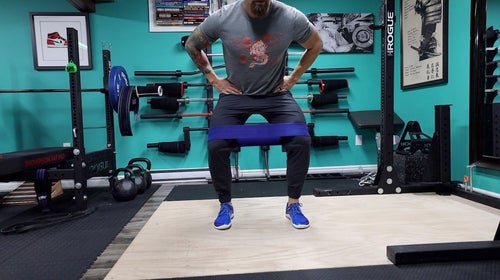 Man in gym with blue band around thighs doing a monster walk.