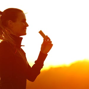 Silhouette of trail runner woman eating energy bar after running at sunset in the mountain
