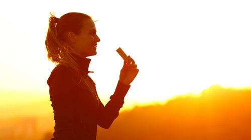 Silhouette of trail runner woman eating energy bar after running at sunset in the mountain