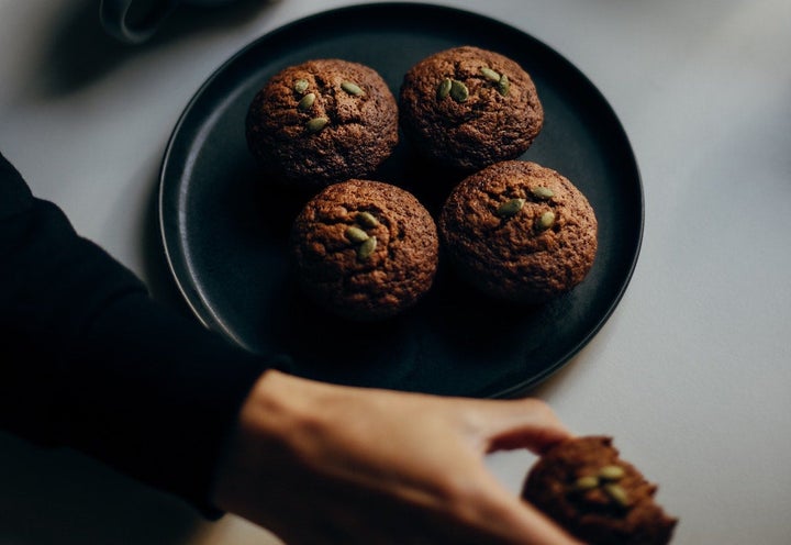 Up close picture of woman's hand grabbing from a place of wholegrain muffins.