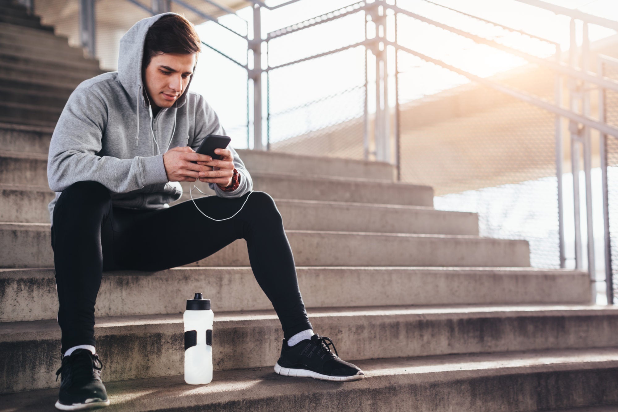 young man sitting on stairs after a run. checking his phone for stats.
