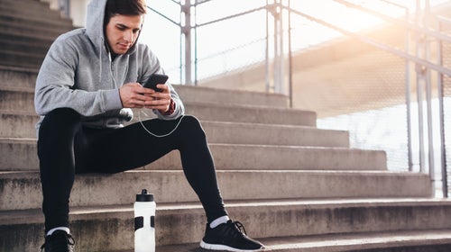 young man sitting on stairs after a run. checking his phone for stats.