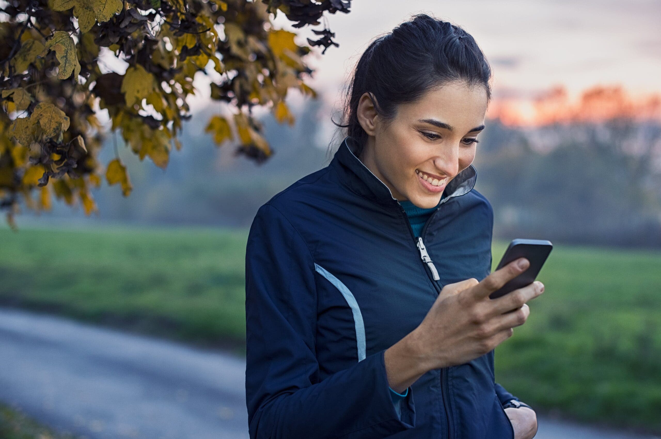 young millenial woman looking at phone post run for running statistics and checking social media.