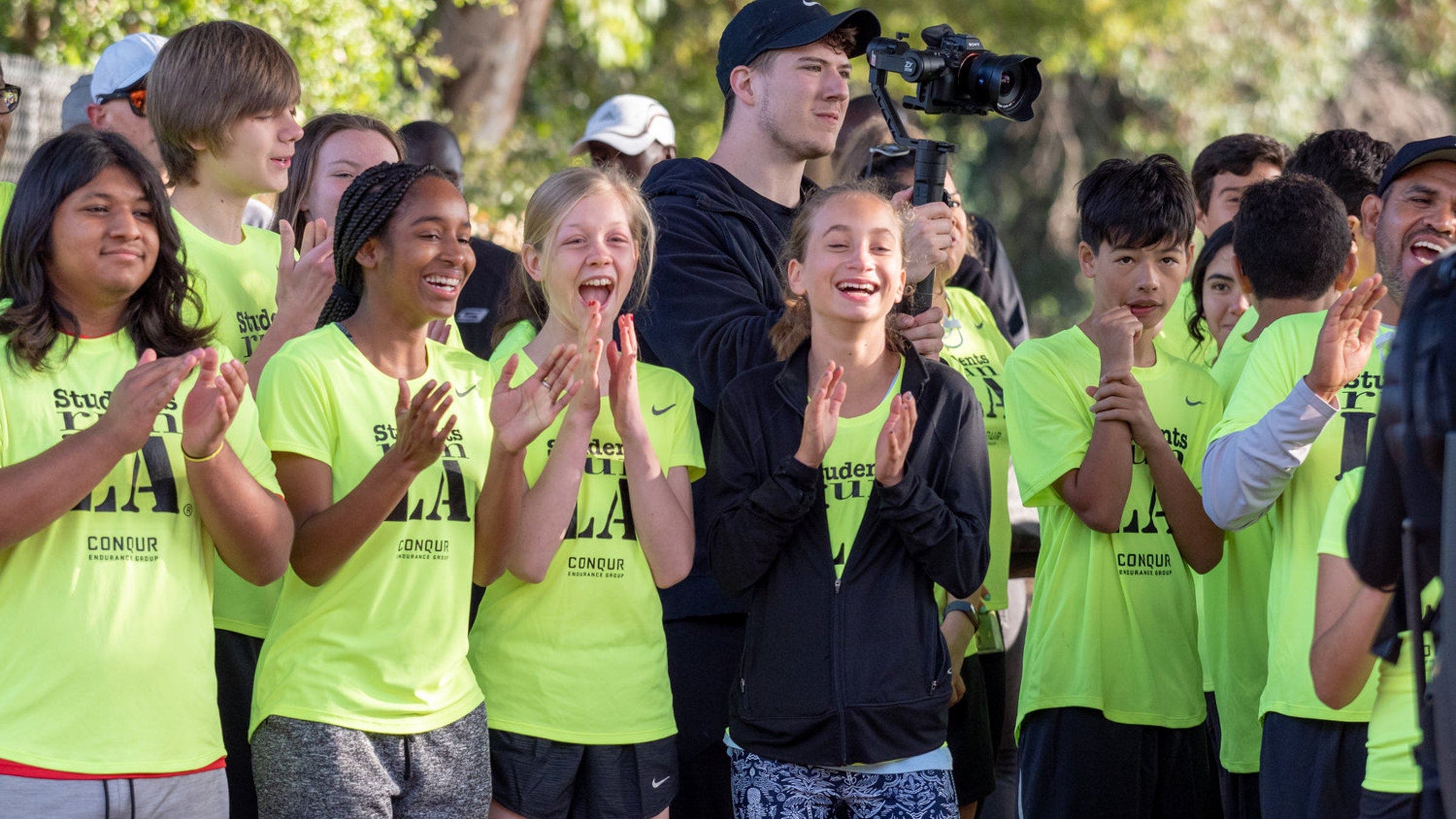 Students stand in a semi-circle in matching shirts and clap