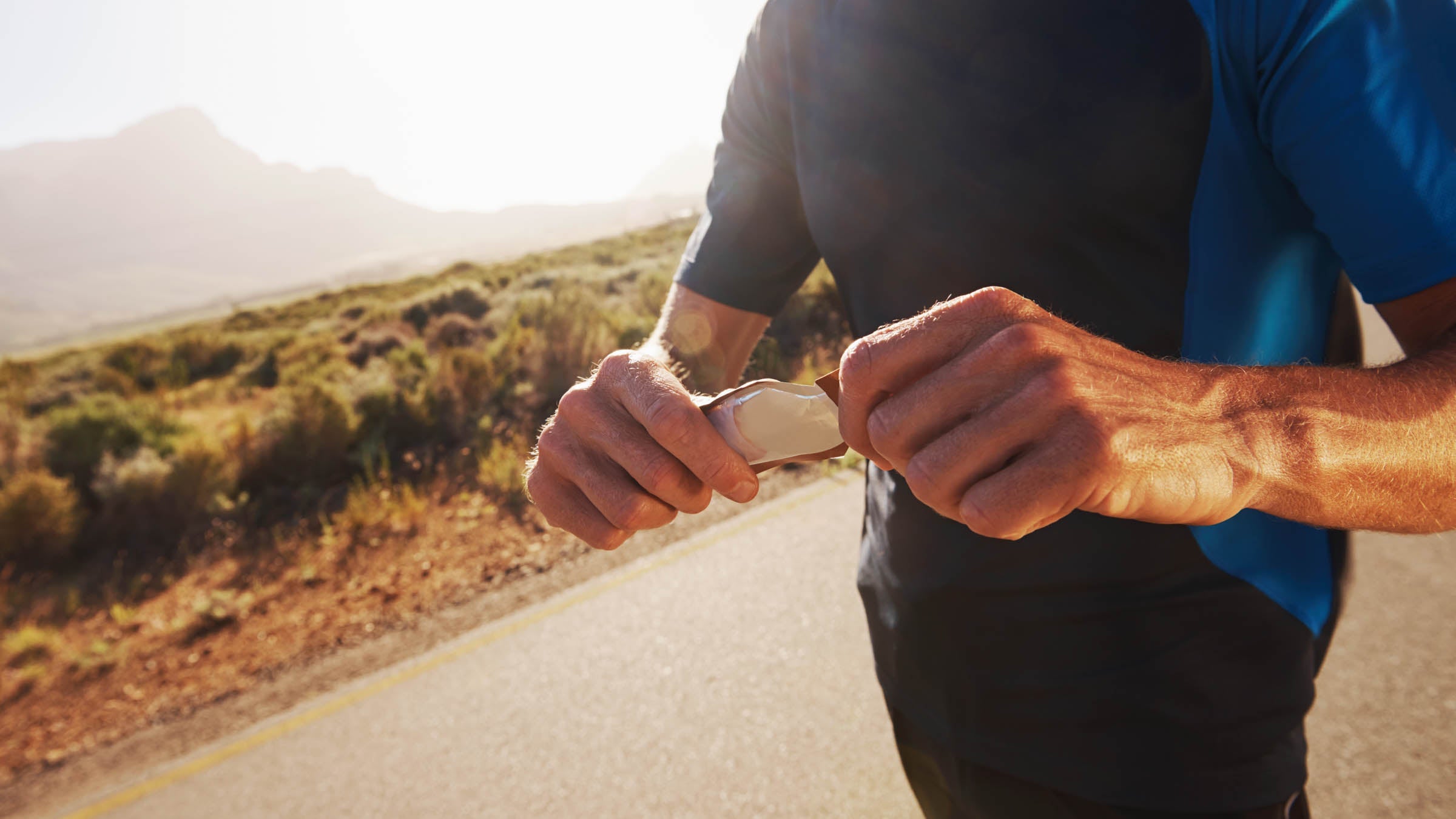 Cropped closeup shot of a male runner unwrapping an energy gel while out on a run in the country
