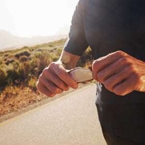Cropped closeup shot of a male runner unwrapping an energy gel while out on a run in the country