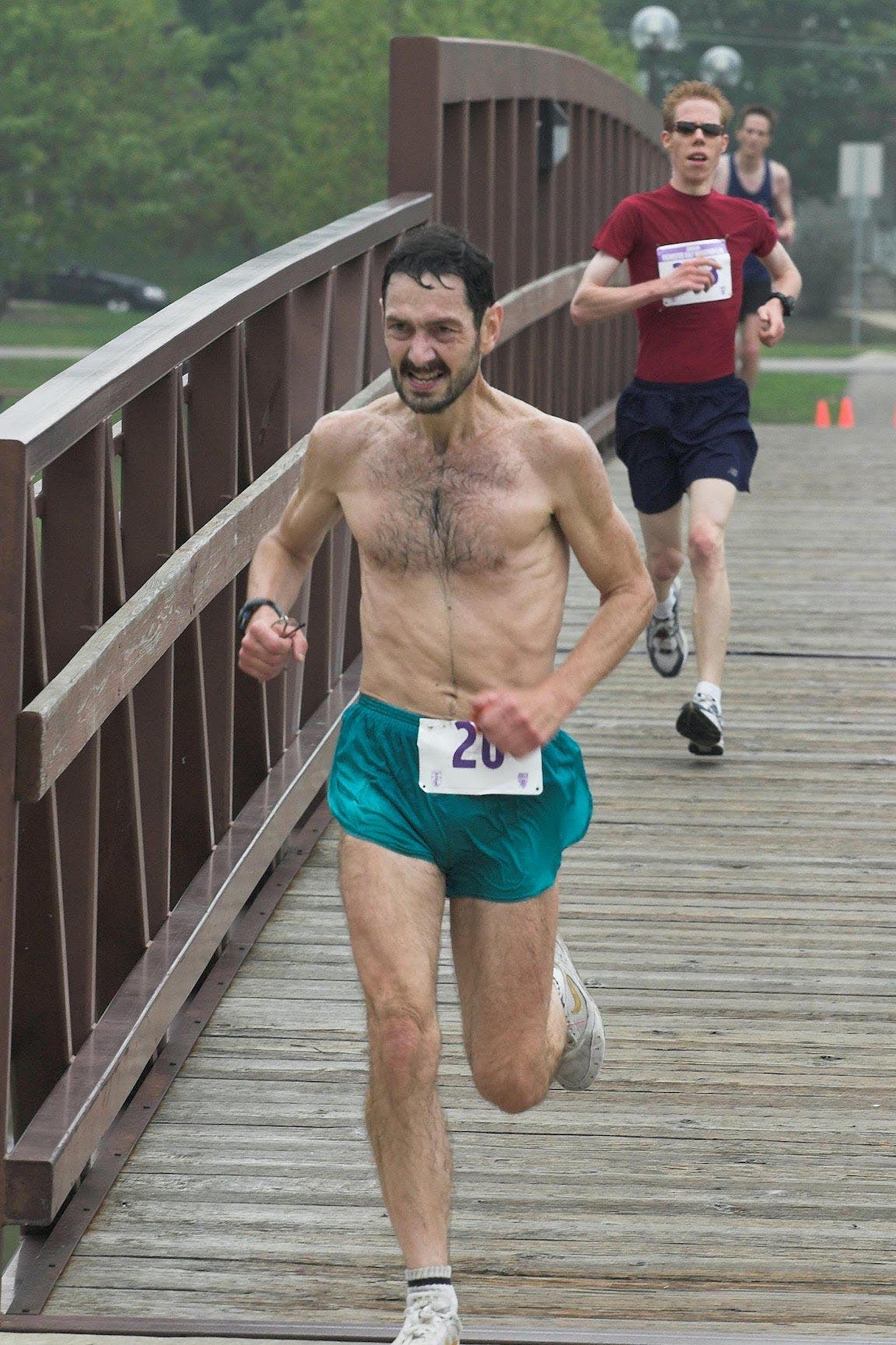 Man racing with shirt off over a bridge.