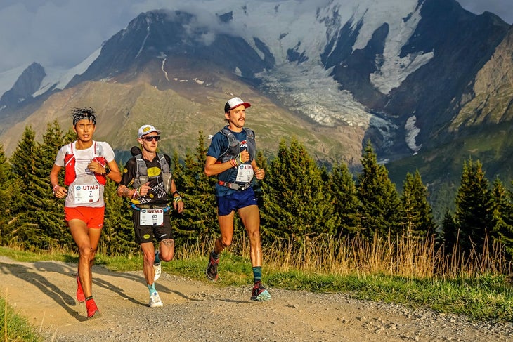 Three male trail runners running on trail with mountains in background.