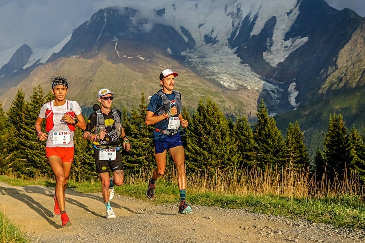 Three male trail runners running on trail with mountains in background.