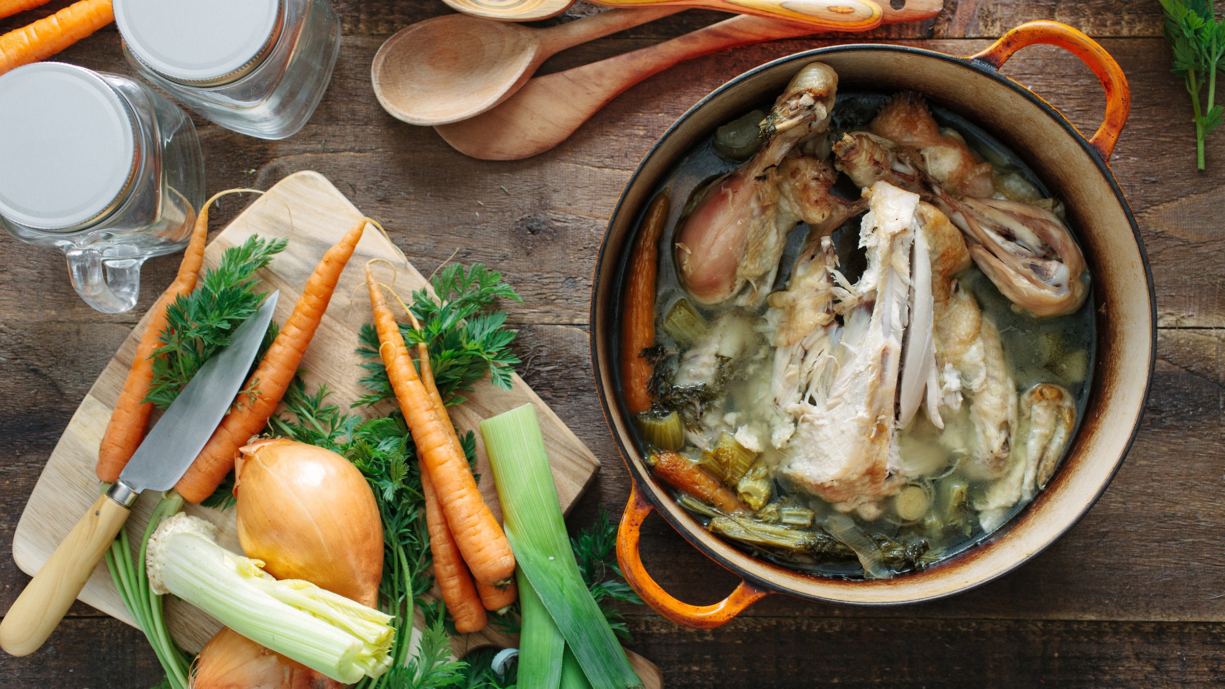Making bone broth, ingredients lay out over a wooden table. Seen from above.