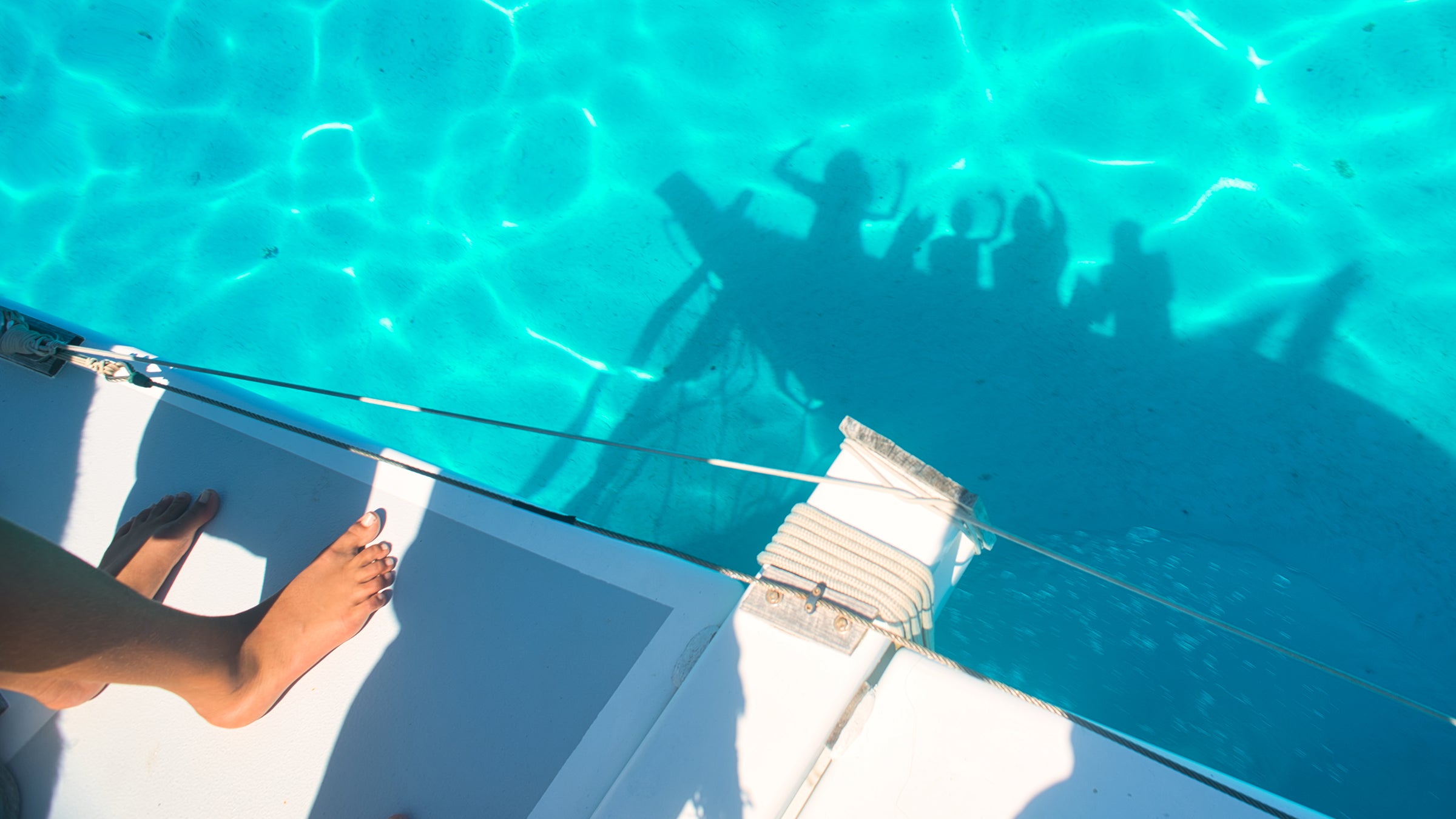 Shadow in water of the author's family waving from their catamaran