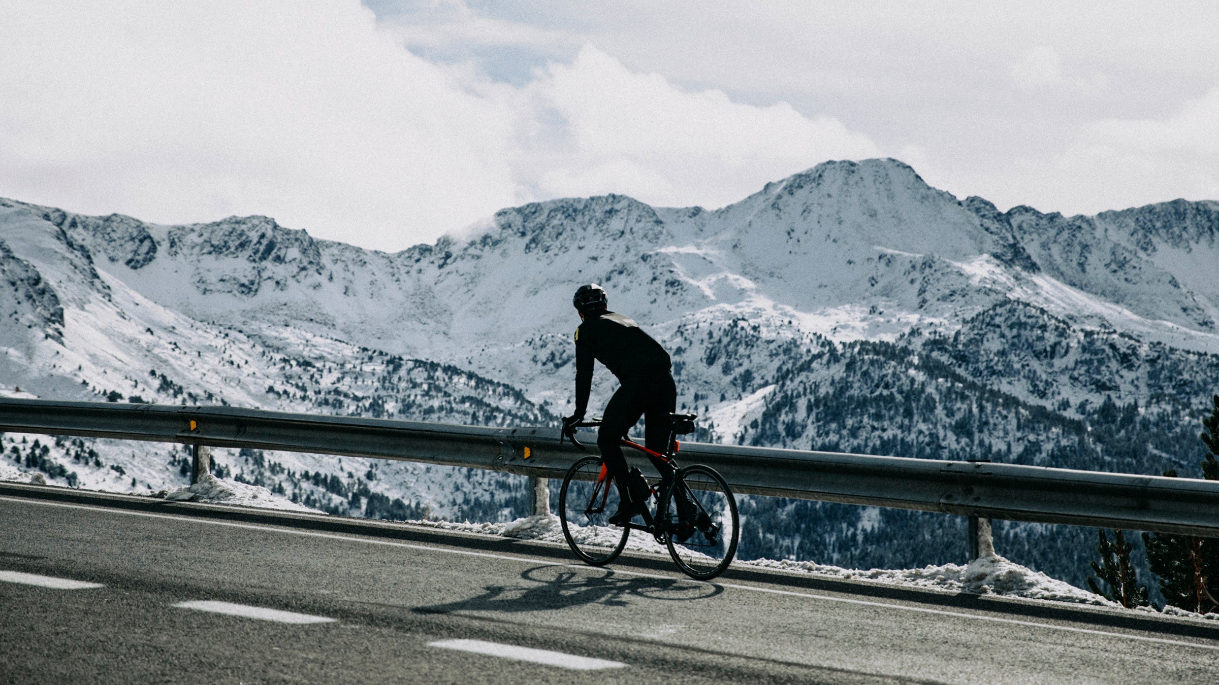 cyclist on mountain road with snowy mountains in the background