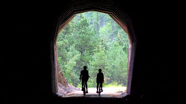 Bicyclists pass through a tunnel in a slate hill, along George S. Mickelson Trail