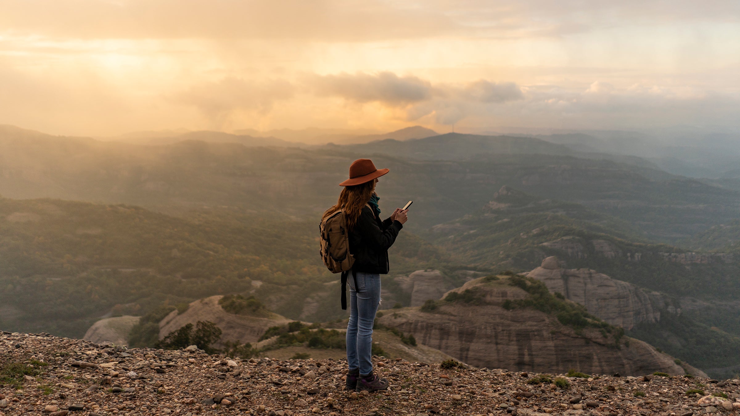 Woman with backback, standing on mountain, looking at view, using smartphone