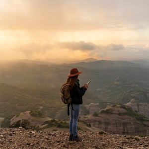 Woman with backback, standing on mountain, looking at view, using smartphone
