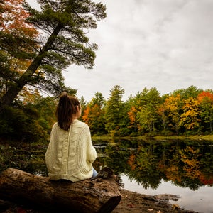 Rear view of woman sitting on tree by lake against sky, Standish, Maine