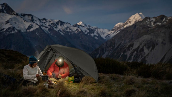 Two people sitting under a tent in the mountains at night