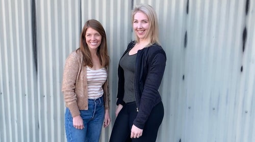two woman standing in front of a steel corrugated wall