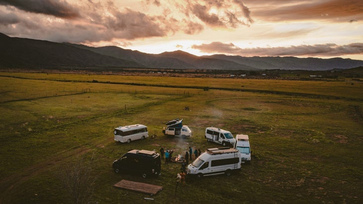 6 campervans parked in a circle in a green field with mountains and clouds in background | Sekr vanlife community