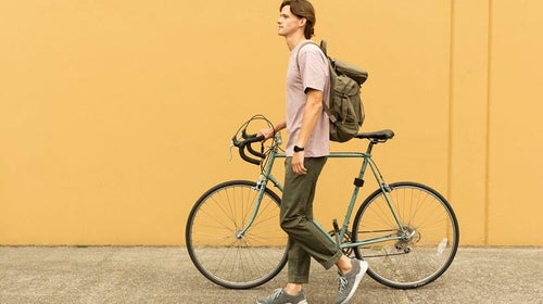 Man walking with bicycle against and orange wall