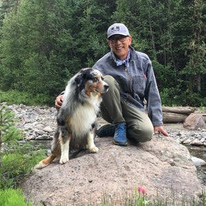 Kim Miller kneeling on a rock with his dog in front of a river