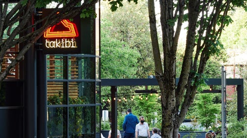 Exterior shot of Snow Peak's takibi restaurant with orange neon sign and trees